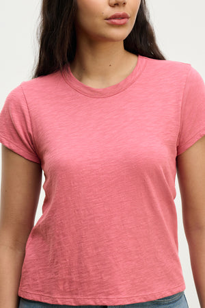 Against a neutral background, a woman stands wearing the MARIE TEE by Velvet by Graham & Spencer, a pink casual tee featuring a relaxed boxy fit.