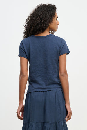 A person with curly hair is wearing the MARIE TEE by Velvet by Graham & Spencer, a navy blue relaxed boxy fit T-shirt and skirt, ideal for a casual occasion.