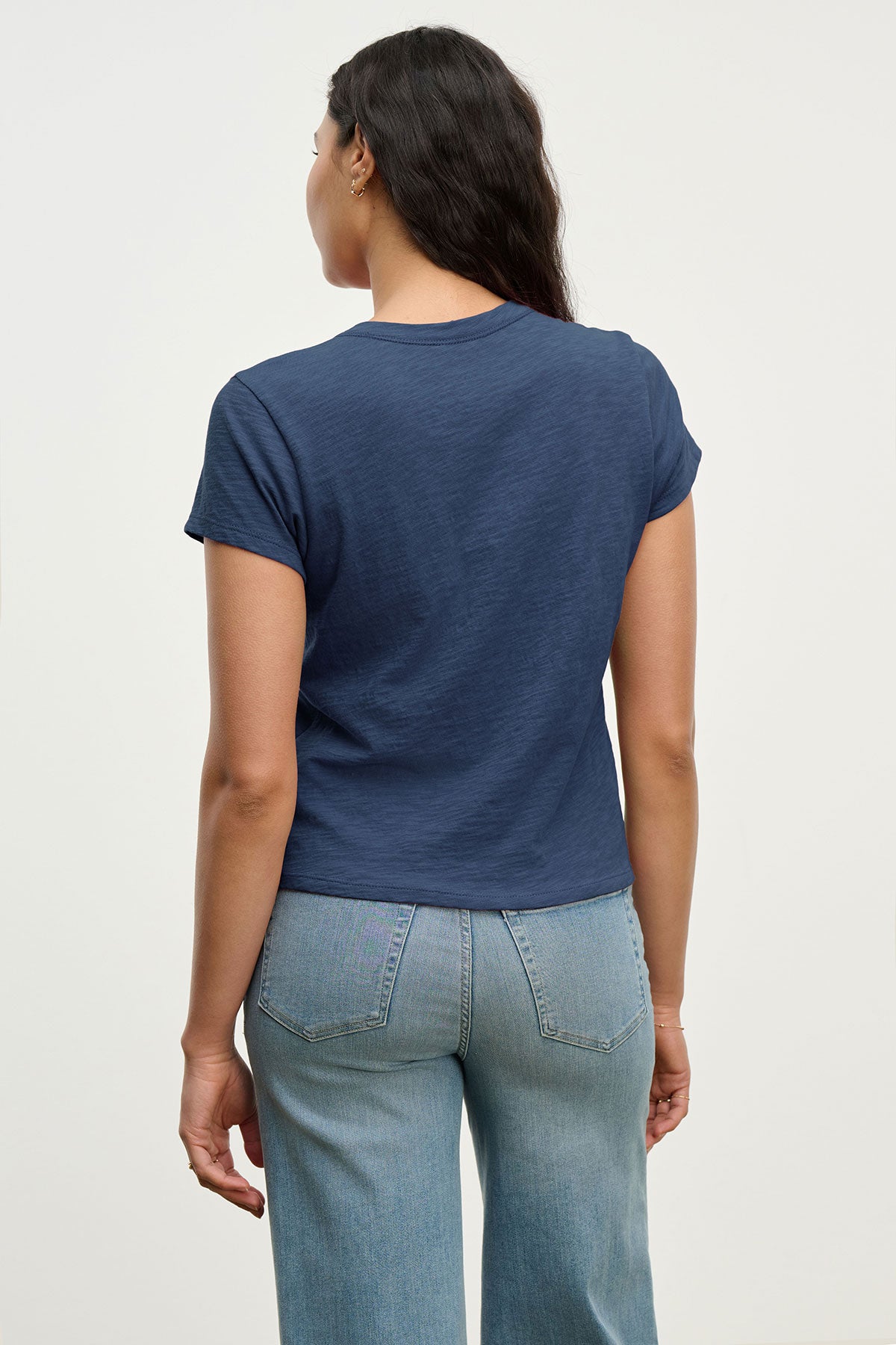   Person wearing a navy blue MARIKA TEE by Velvet by Graham & Spencer in a relaxed boxy fit with light blue jeans, standing with their back to the camera against a plain background. 