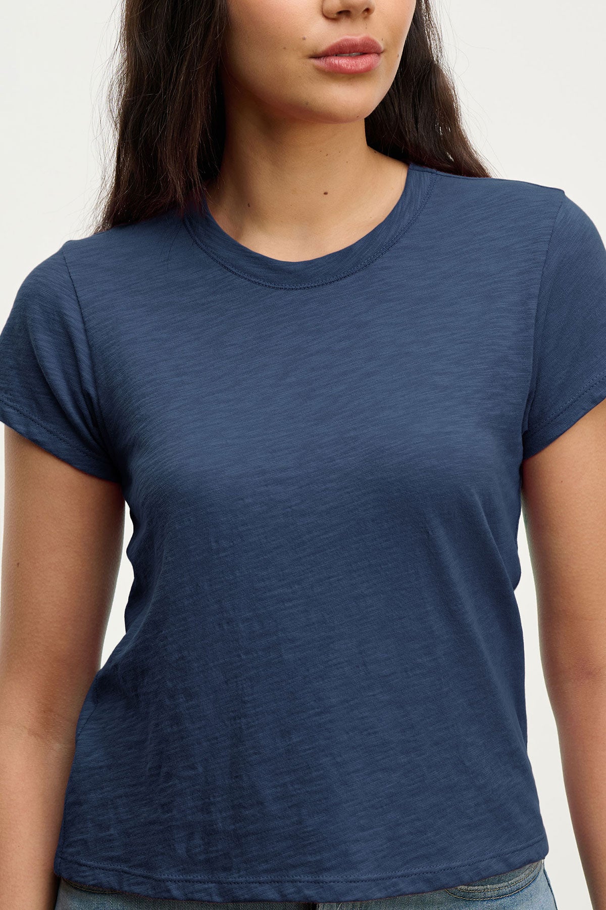   A woman wears the MARIKA TEE by Velvet by Graham & Spencer, a navy blue cotton slub short-sleeve t-shirt with a relaxed boxy fit, shown from shoulders to waist against a light background. 