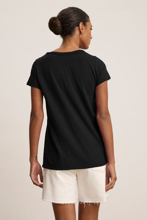 A person stands with their back to the camera, wearing the TILLY TEE by Velvet by Graham & Spencer, a classic crew neck made from soft cotton slub, paired with white shorts against a plain background.