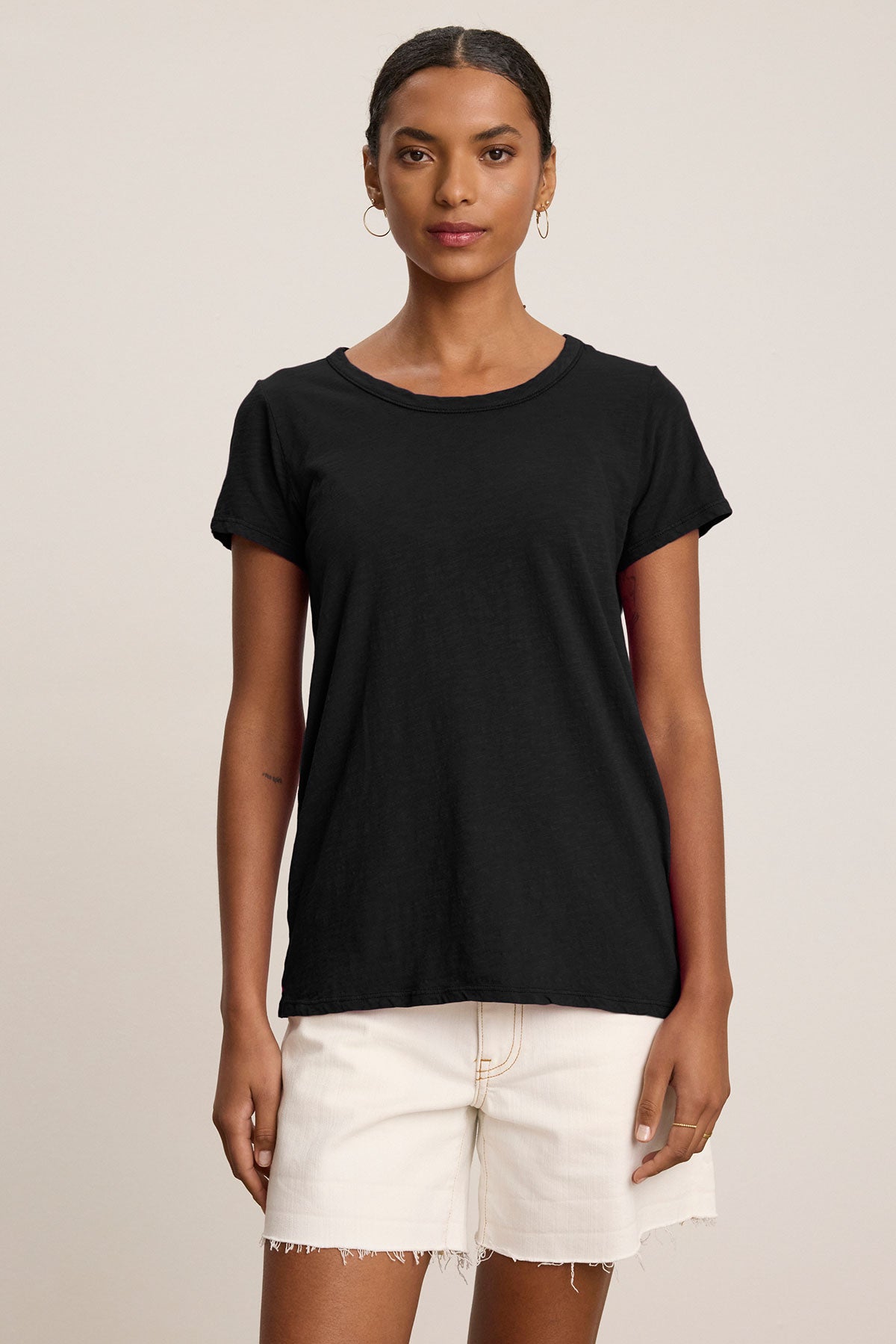   A woman wearing the TILLY TEE by Velvet by Graham & Spencer in black and off-white frayed shorts stands against a neutral background. 