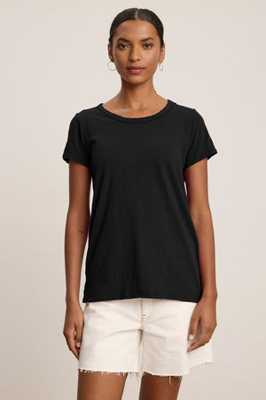 A woman wearing the TILLY TEE by Velvet by Graham & Spencer in black and off-white frayed shorts stands against a neutral background.