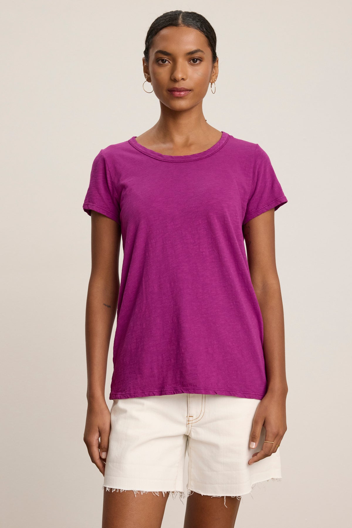 A person faces the camera wearing the TILLY TEE by Velvet by Graham & Spencer, a classic crew neck crafted from soft cotton slub, paired with white shorts against a plain light background.-39111855964353