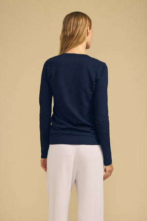 A person stands with their back to the camera against a plain beige background, wearing the Velvet by Graham & Spencer BLAIRE TEE in navy cotton slub and loose white pants.
