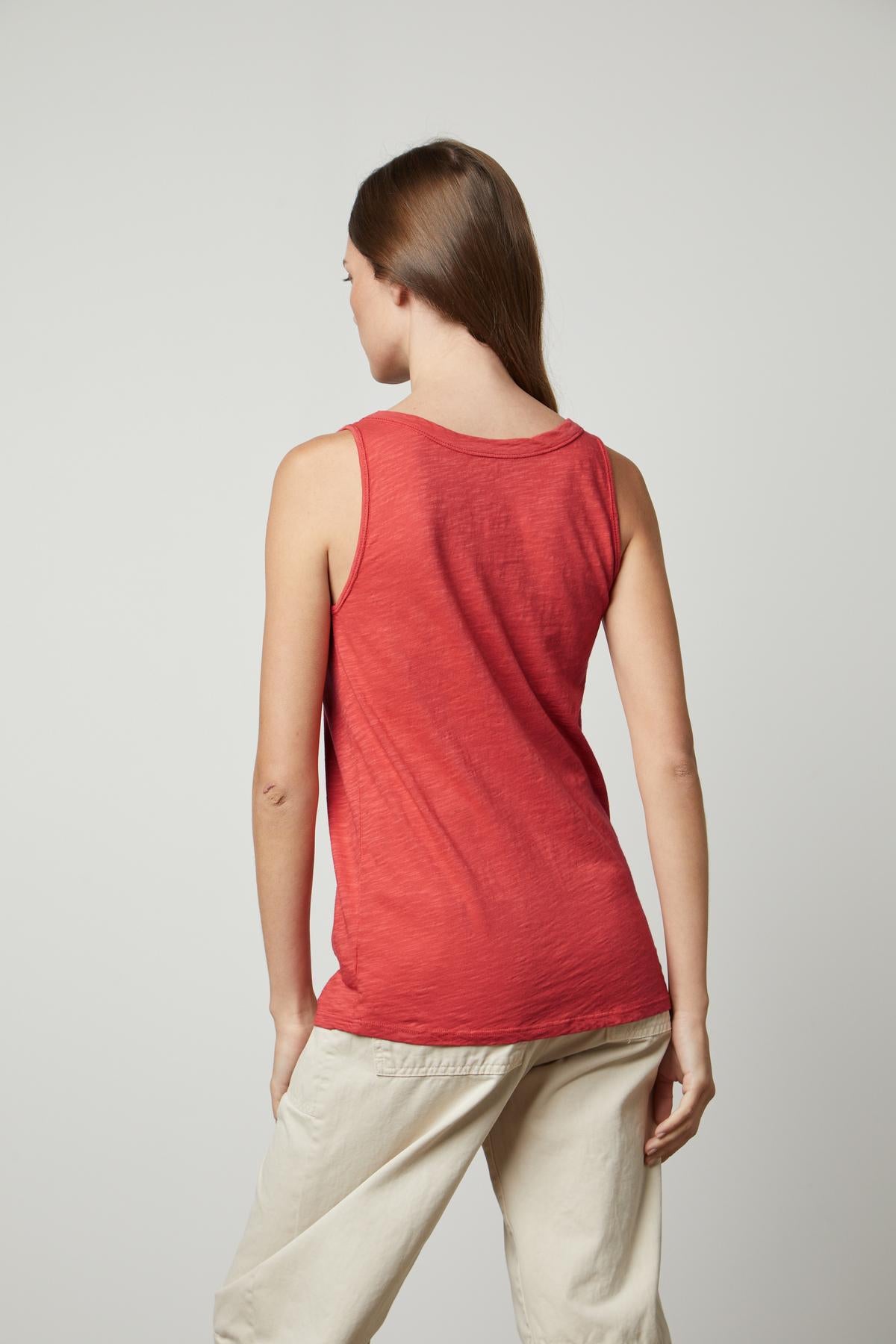   The back view of a woman wearing a red Velvet by Graham & Spencer tank top and tan pants, with flattering arm hole. 