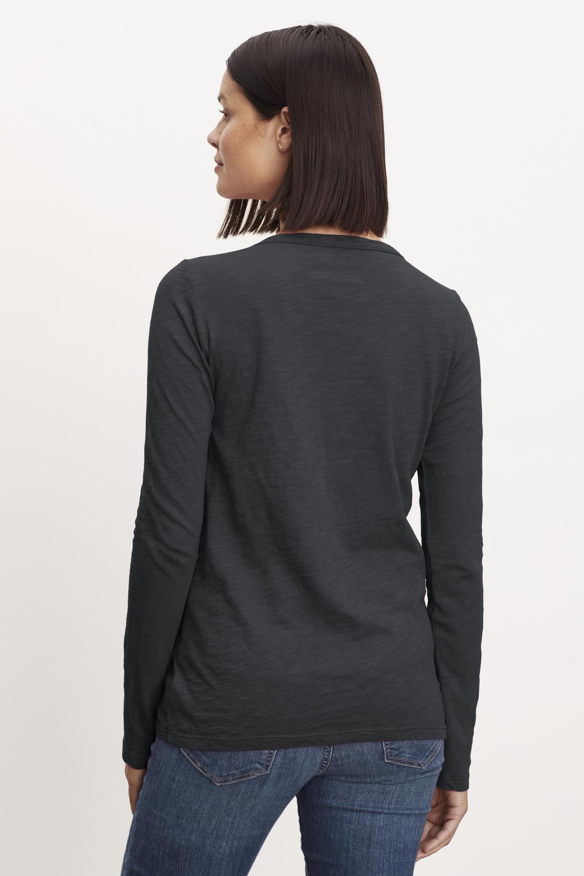   The back view of a woman wearing LIZZIE ORIGINAL SLUB LONG SLEEVE TEE by Velvet by Graham & Spencer jeans and a long-sleeved shirt. 