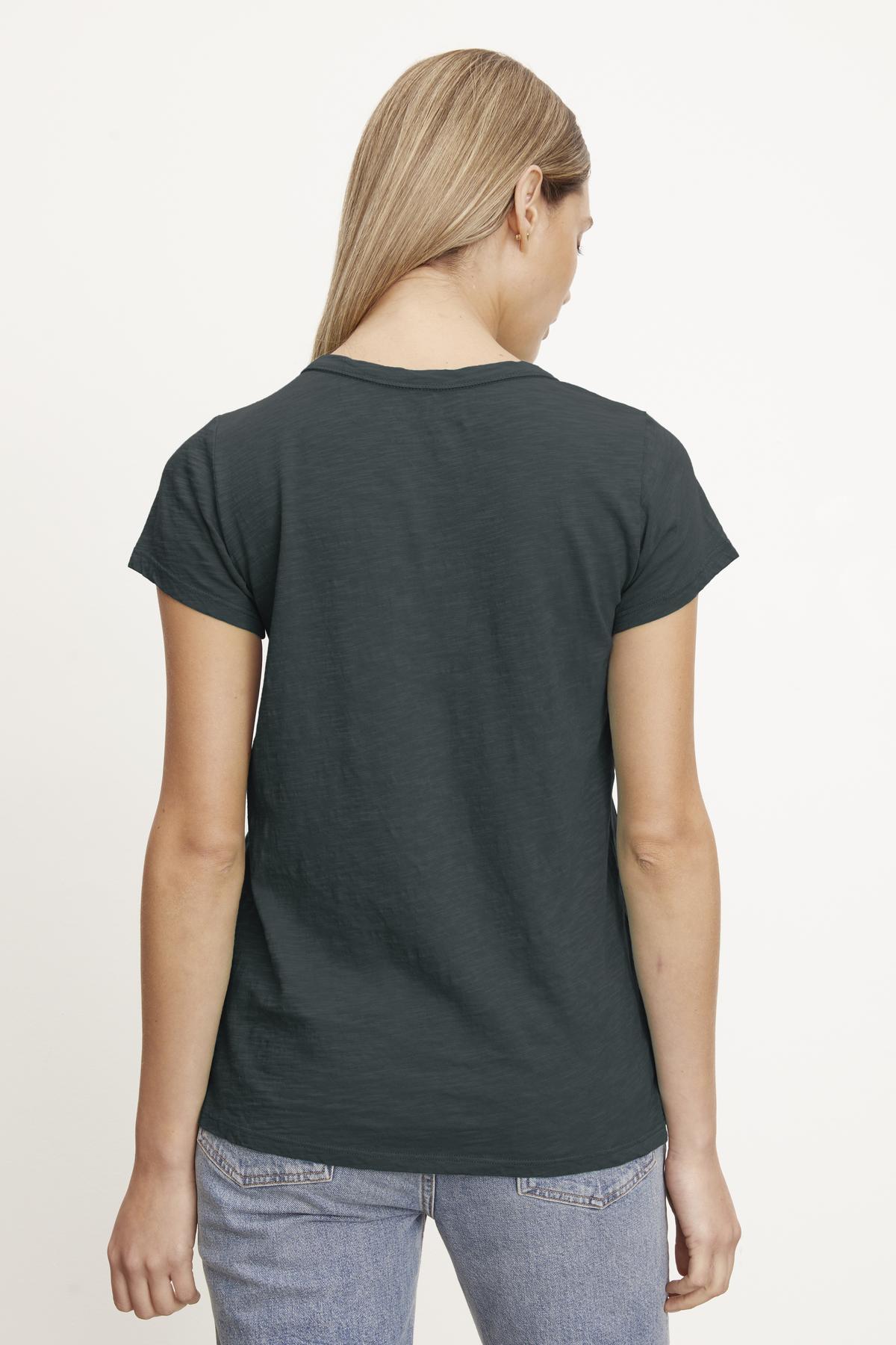   A person with long blonde hair is shown from the back, wearing a dark gray TILLY TEE by Velvet by Graham & Spencer made of soft cotton slub and light blue jeans against a plain white background—a true California classic. 