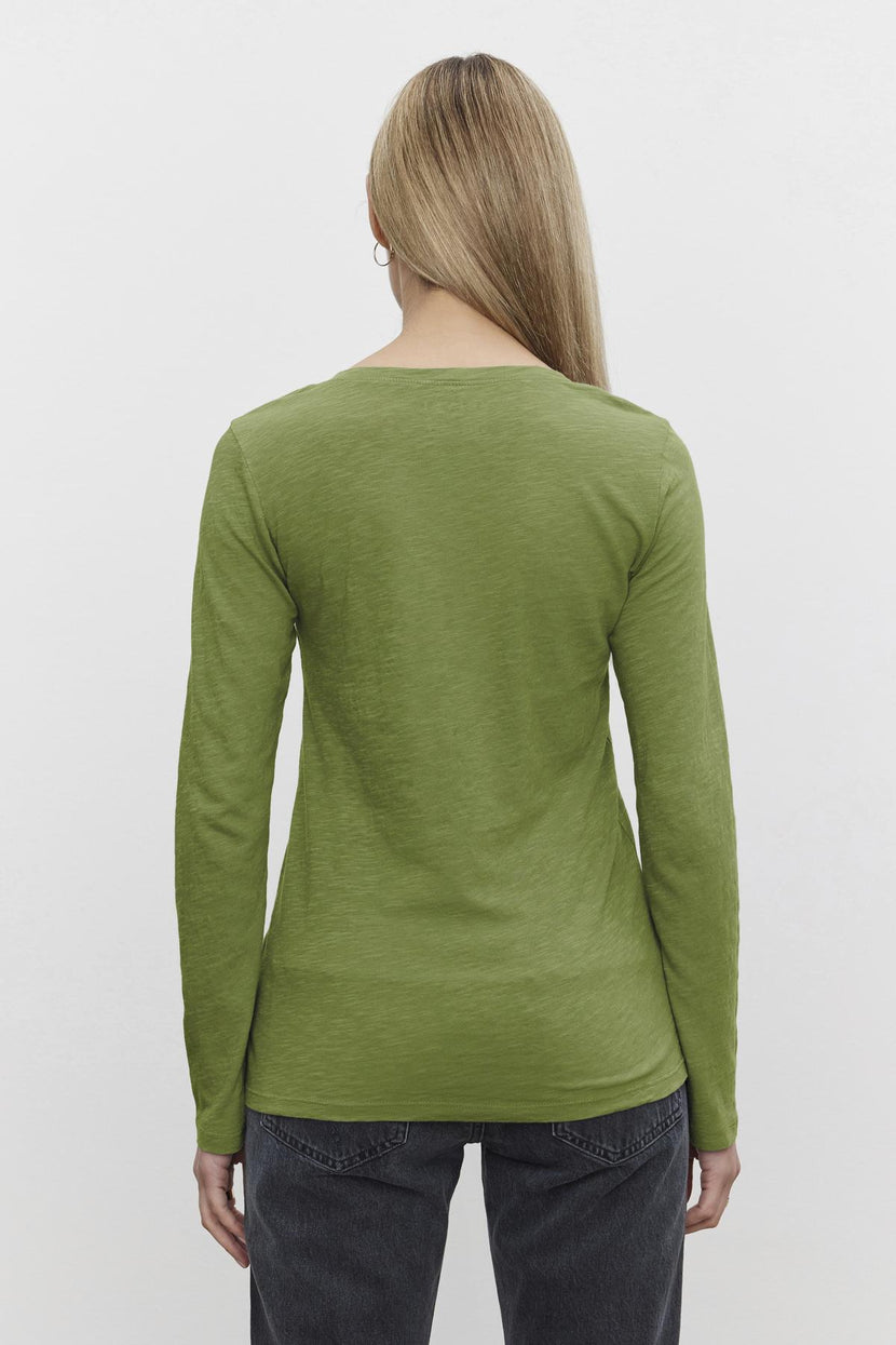 A person with long hair is seen from behind wearing a Velvet by Graham & Spencer's BLAIRE TEE, a green cotton slub shirt featuring an effortless v-neckline, paired with dark pants, against a plain white background.