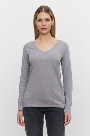 A person with long hair wearing the BLAIRE TEE from Velvet by Graham & Spencer—a gray, textured cotton slub V-neck shirt—and dark jeans stands facing forward against a plain white background.