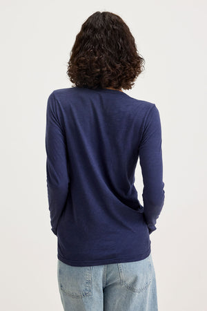 A person with curly hair, wearing a Velvet by Graham & Spencer BLAIRE TEE shirt in navy made of textured cotton slub and light blue jeans, is shown from the back against a plain background.