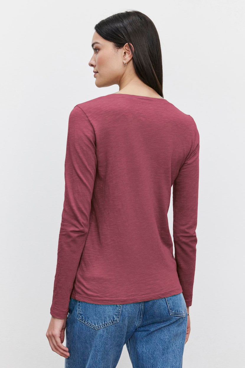 A person with long hair is wearing the maroon BLAIRE TEE from Velvet by Graham & Spencer and blue jeans, facing away from the camera against a plain white background.