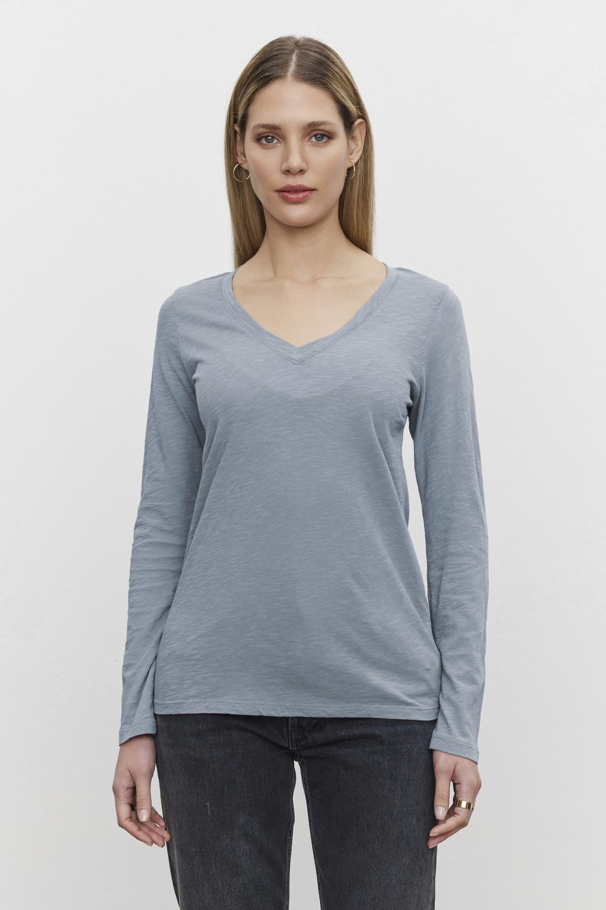   A person with long hair is wearing a light blue BLAIRE TEE from Velvet by Graham & Spencer and dark jeans, standing against a plain white background. 