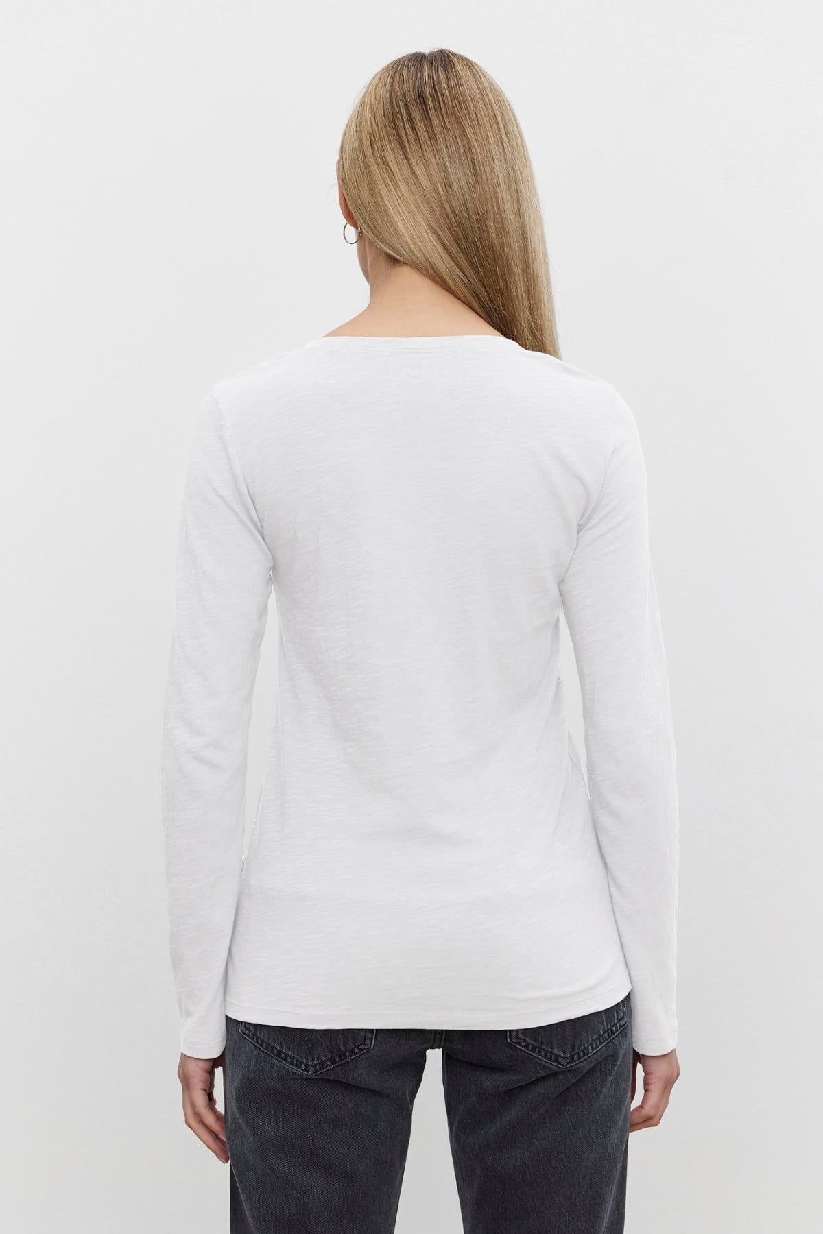   A person with long, straight hair wearing a white BLAIRE TEE by Velvet by Graham & Spencer and dark jeans is shown from the back against a plain background. 