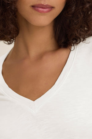 Close-up of a woman wearing the BLAIRE TEE by Velvet by Graham & Spencer—a white cotton slub V-neck tee—showing her neck, lower face, and curly hair.