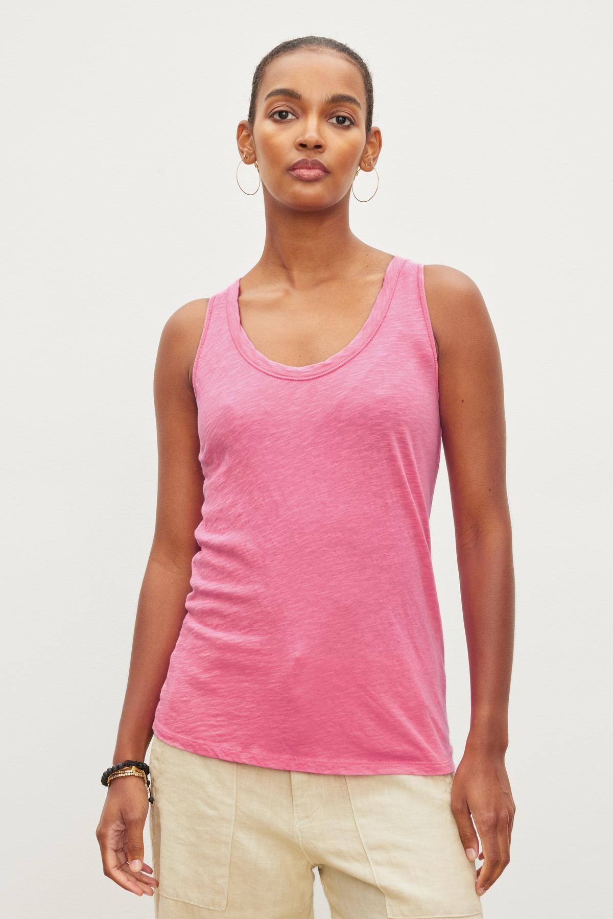   A person wearing a JOY ORIGINAL SLUB SCOOP NECK TANK by Velvet by Graham & Spencer with a soft cotton texture and beige pants stands against a plain white background. With an easy silhouette that includes flattering arm holes, they are looking directly at the camera. 