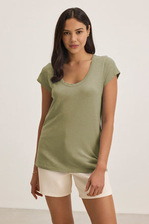 A woman stands against a plain background wearing the KIRA TEE by Velvet by Graham & Spencer, a light green cotton slub fabric t-shirt with cap sleeves, paired with off-white shorts.