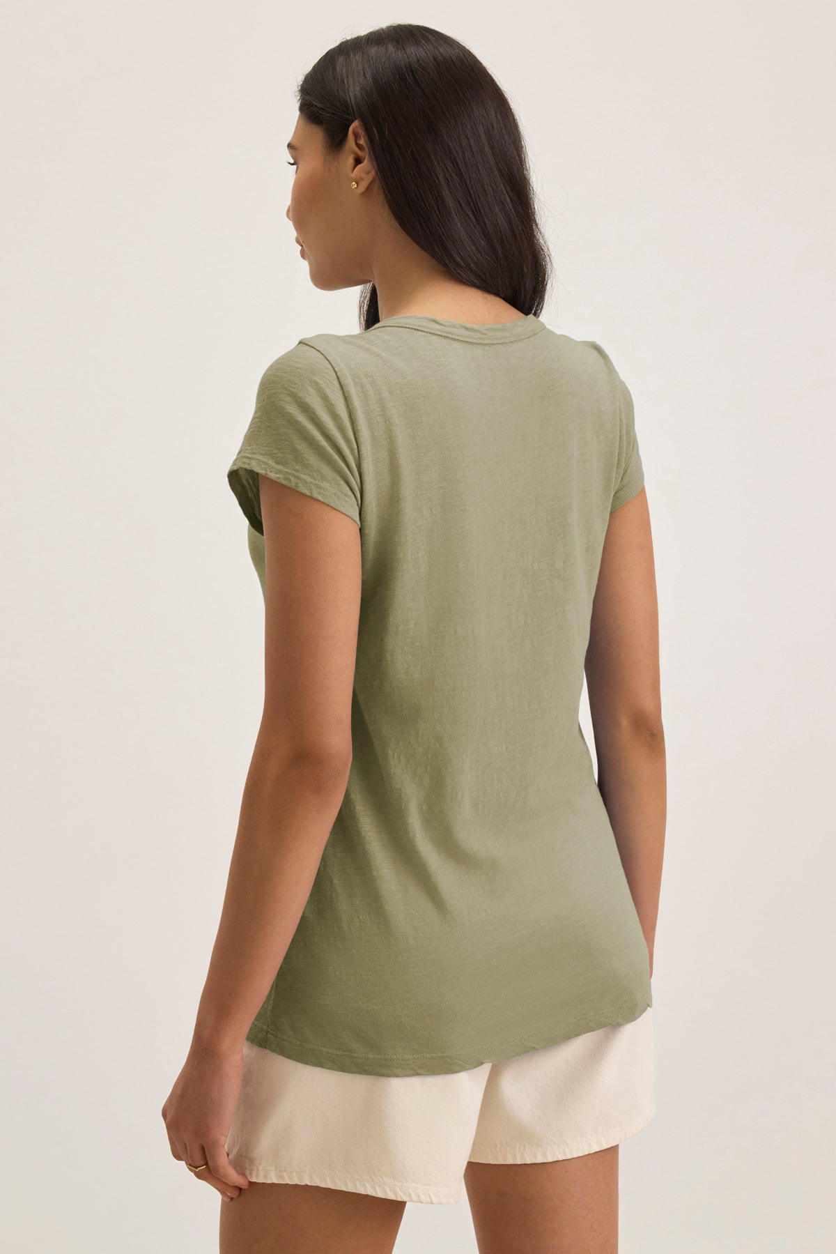 A woman with long dark hair, seen from behind, wears the KIRA TEE by Velvet by Graham & Spencer in light green and off-white shorts against a plain background.-39149282525377