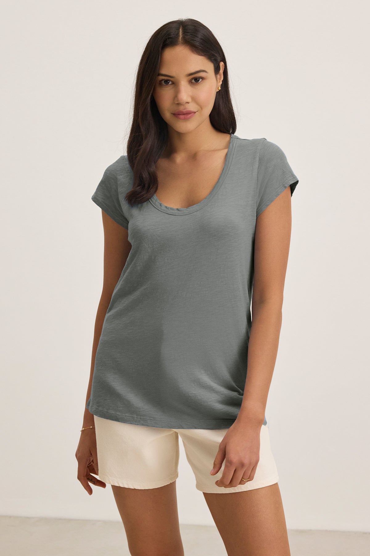   The woman wears Velvet by Graham & Spencer's KIRA TEE, a gray cotton slub t-shirt with a scoop neckline, paired with light shorts against a plain background, highlighting casual style with subtle texture. 