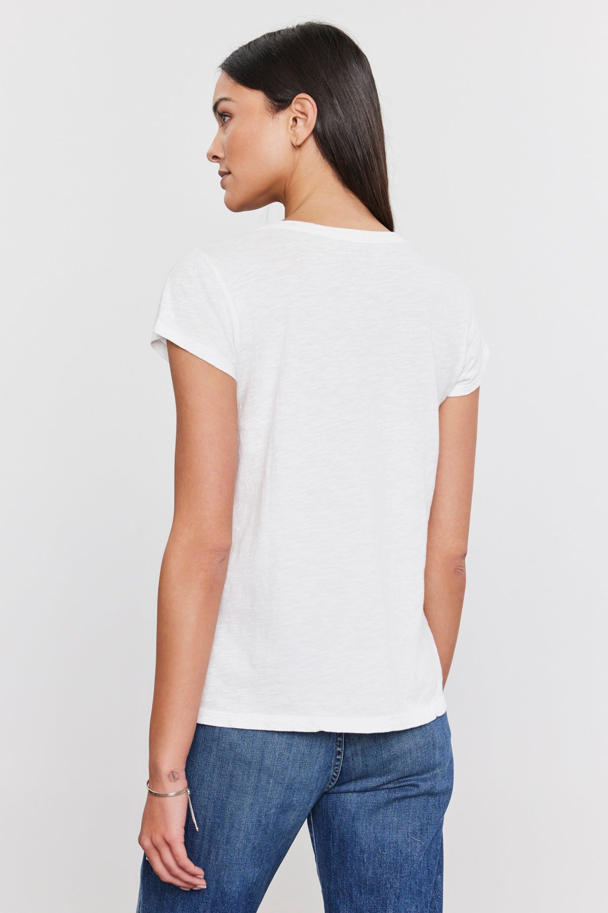The back view of a woman wearing a white Velvet by Graham & Spencer KIRA ORIGINAL SLUB SCOOP NECK TEE and jeans.-35586106032321