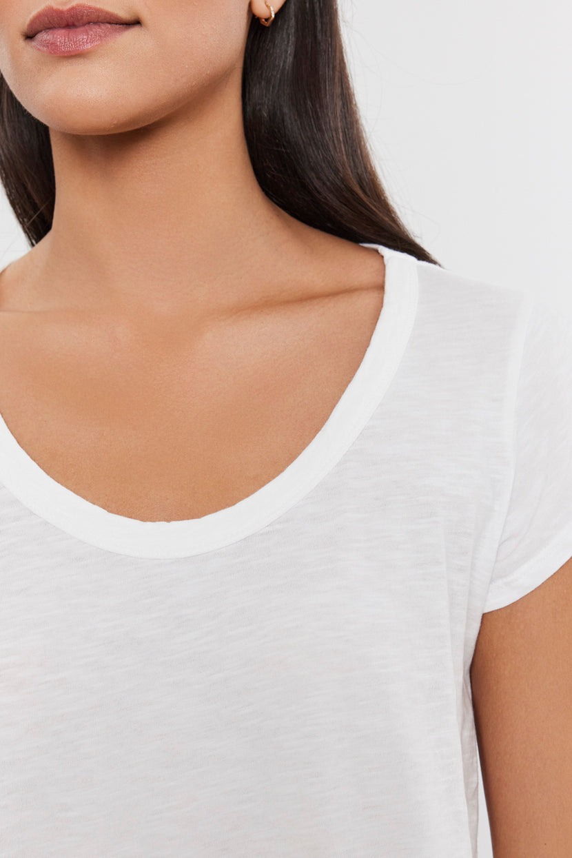 Close-up of a person wearing a plain white KIRA TEE by Velvet by Graham & Spencer. Made from soft cotton slub fabric, this piece is perfect for everyday wear. The image shows their neck, shoulders, and part of their face with dark, straight hair.