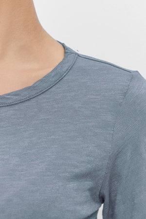 Close-up of a person in the LIZZIE TEE by Velvet by Graham & Spencer, featuring a classic crew neckline and textured cotton slub fabric in light blue with long sleeves.