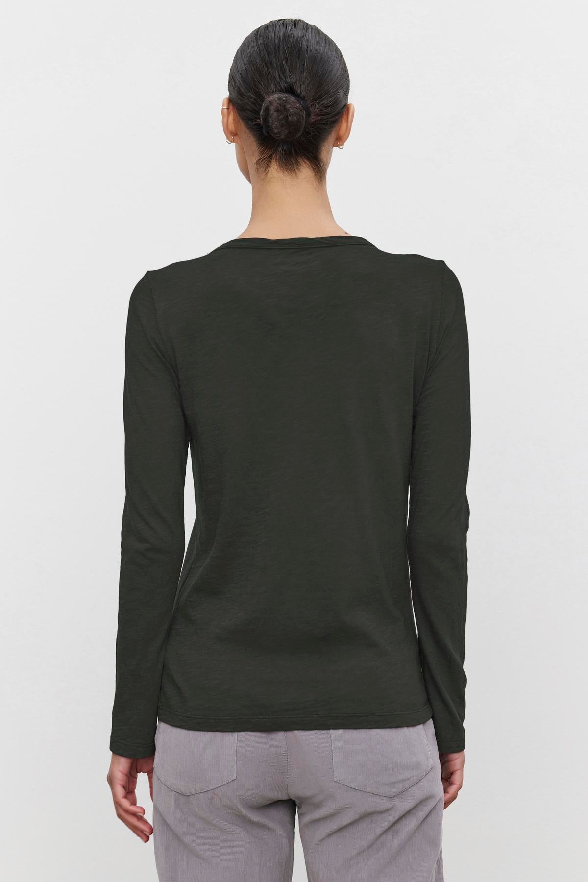   Someone with their hair in a bun is wearing the LIZZIE TEE, a long-sleeved dark green shirt by Velvet by Graham & Spencer, crafted from textured cotton slub. They are also wearing light gray pants, and the view is from behind. 