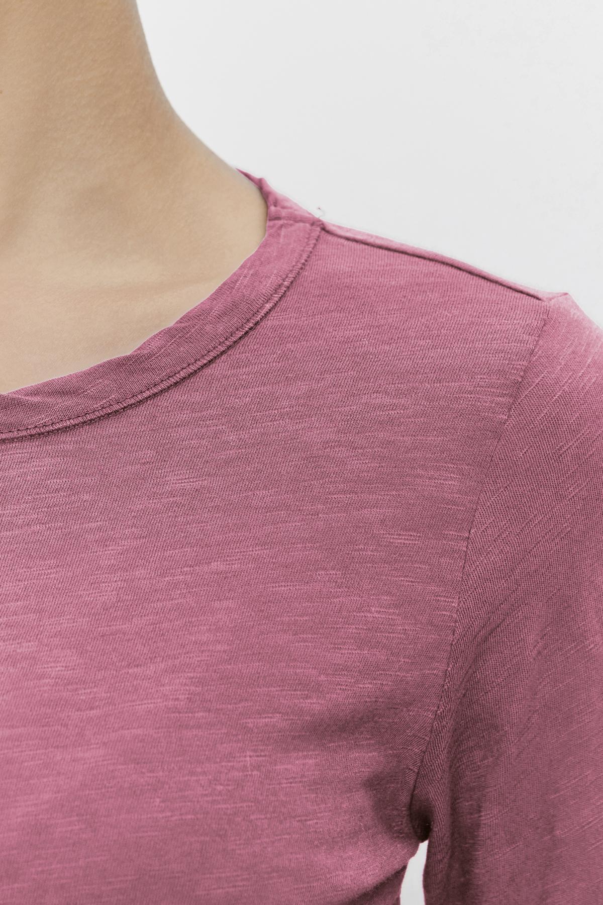   Close-up of a person wearing the LIZZIE TEE by Velvet by Graham & Spencer, featuring a pink color and classic crew neckline with highlighted shoulder detail. 