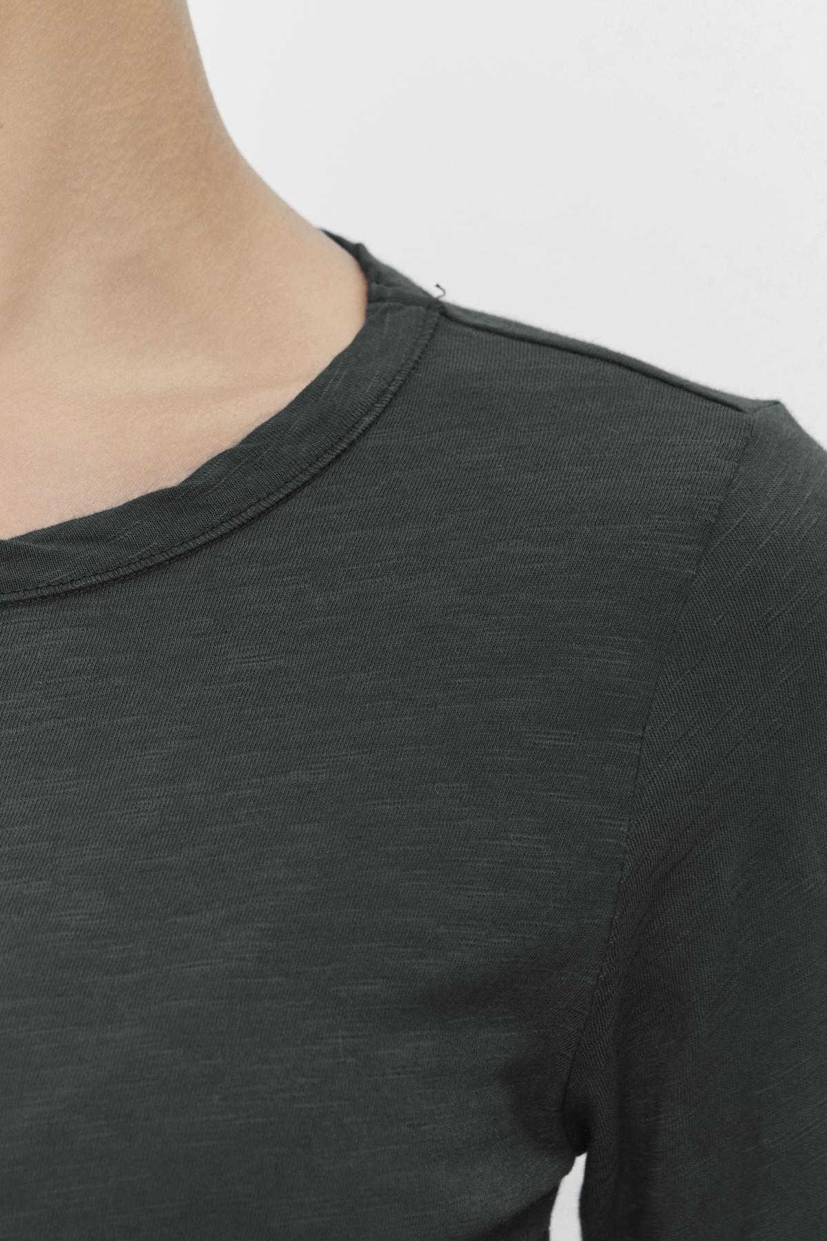   Close-up of a person wearing the Velvet by Graham & Spencer LIZZIE TEE, crafted from soft cotton slub in a dark green shade. The focus is on the shoulder and upper chest area, highlighting the round neckline and long sleeves. 