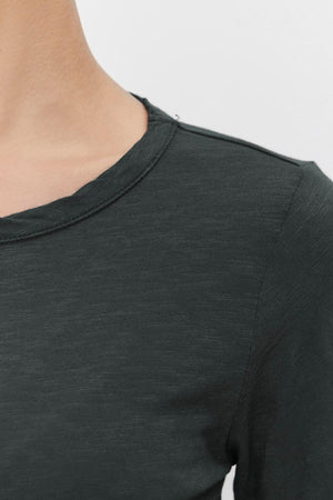 Close-up of a person wearing the Velvet by Graham & Spencer LIZZIE TEE, crafted from soft cotton slub in a dark green shade. The focus is on the shoulder and upper chest area, highlighting the round neckline and long sleeves.