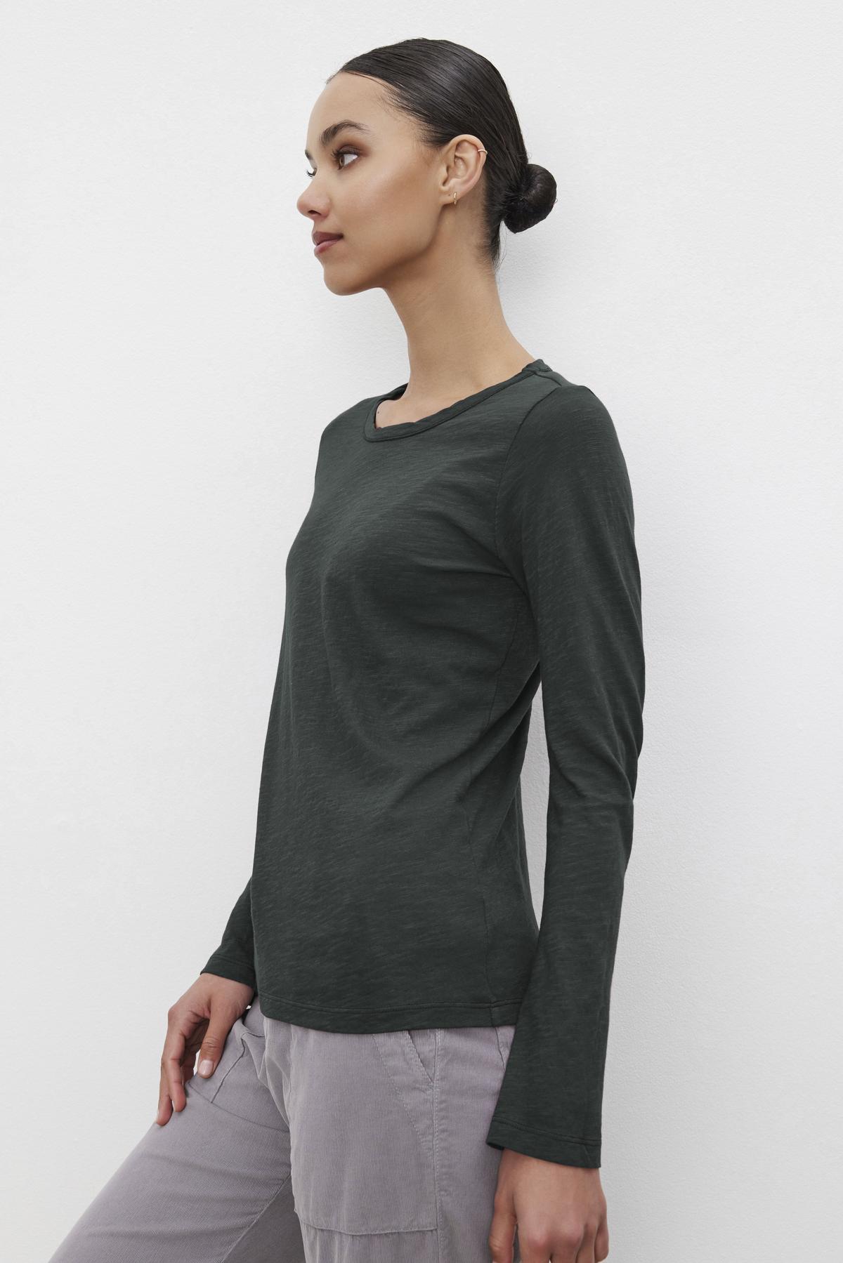 Someone wearing the LIZZIE TEE, a dark green long-sleeve shirt with a crew neckline from Velvet by Graham & Spencer, stands against a plain white background.-38139494334657