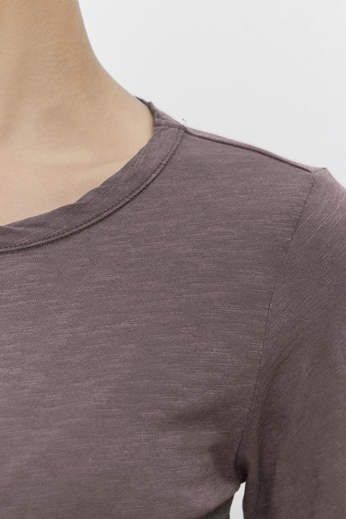   Close-up of a person wearing the LIZZIE TEE, a brown, slightly heathered, long-sleeved shirt from Velvet by Graham & Spencer. The focus is on the upper shoulder and the classic crew neckline of this textured cotton slub tee. The background is plain white. 