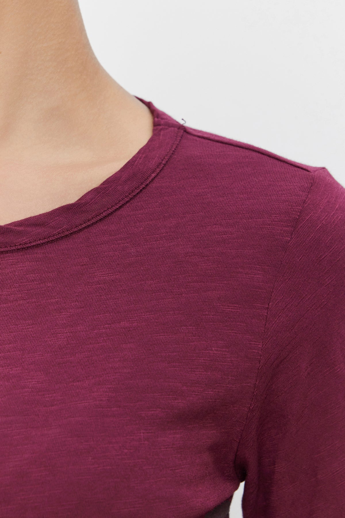   Close-up view of a person wearing the LIZZIE TEE by Velvet by Graham & Spencer, featuring a plain, maroon-colored design with short sleeves and a simple, classic crew neckline. 