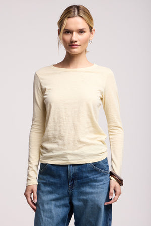 A person wears the LIZZIE TEE by Velvet by Graham & Spencer, a light-colored long sleeve crew neck top, paired with blue jeans, standing facing forward against a plain background.
