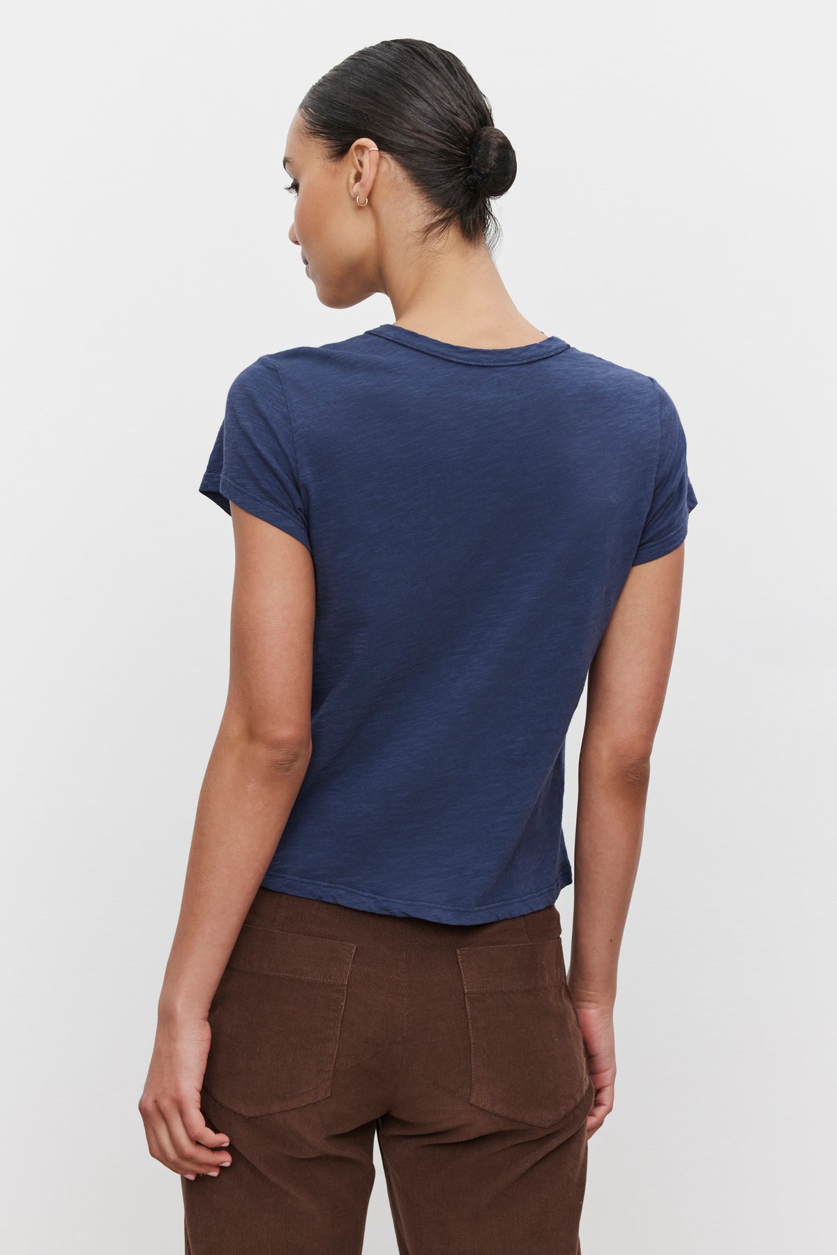   A person with short dark hair is shown from the back wearing the MARIE TEE by Velvet by Graham & Spencer, a navy blue cotton slub t-shirt with a boxy fit, paired with brown pants, making for a perfect casual look. 