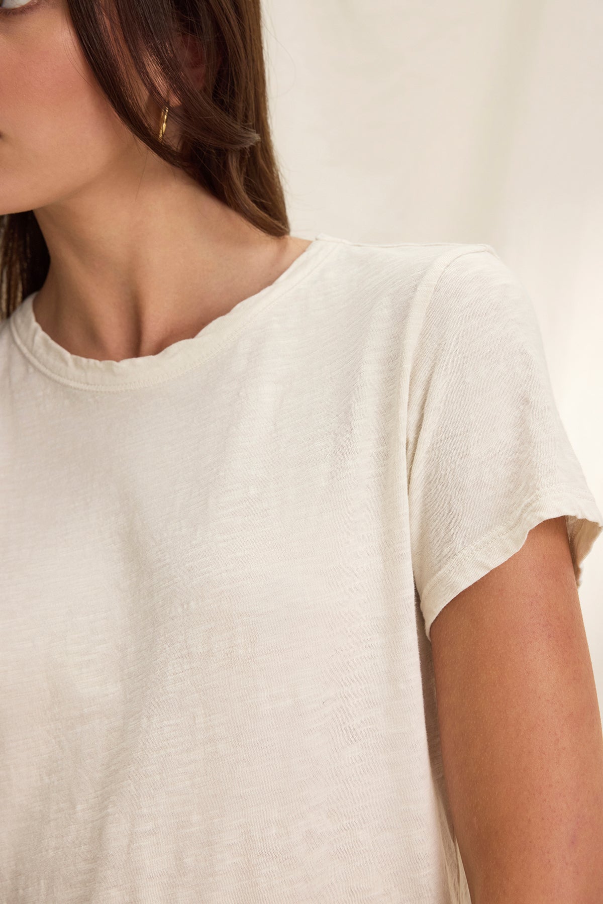   A person wearing a MARIE TEE from Velvet by Graham & Spencer, with a beige boxy fit and gold hoop earrings, stands against a neutral background, perfect for casual occasions. 