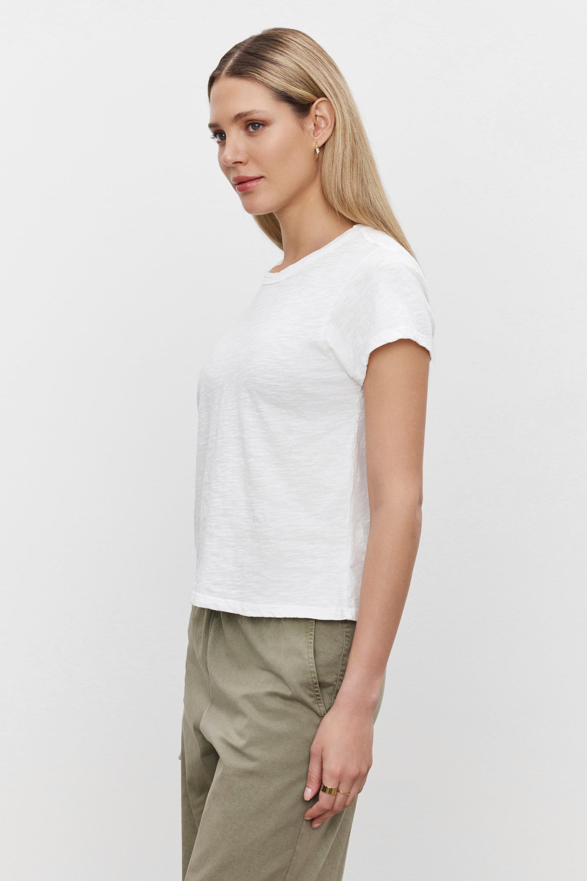   A person with long blonde hair, dressed for a casual occasion in the MARIE TEE by Velvet by Graham & Spencer and khaki pants, is shown in side profile against a plain white background. 