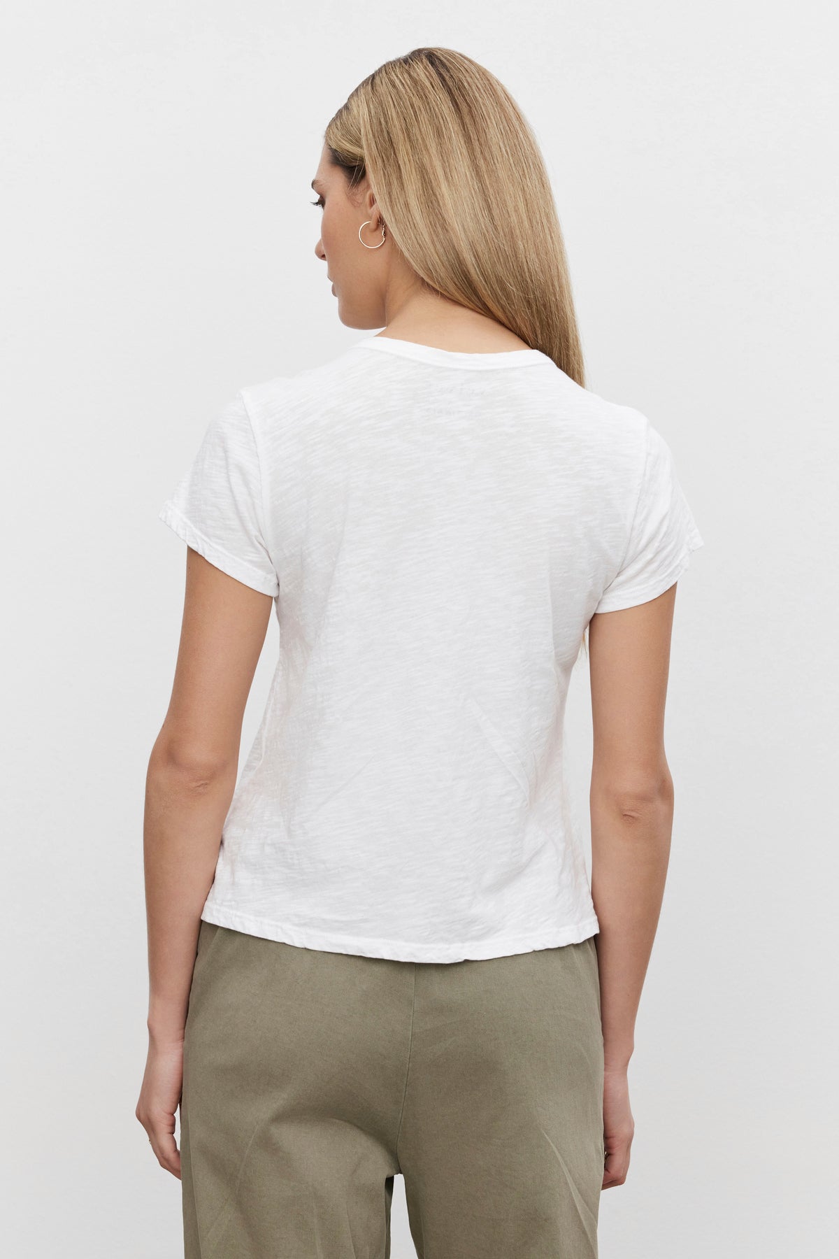   A person with long, straight hair wears the MARIE TEE by Velvet by Graham & Spencer—a white short-sleeve cotton slub shirt—paired with green pants in a relaxed boxy fit, seen from the back against a plain white background. Perfect for any casual occasion. 