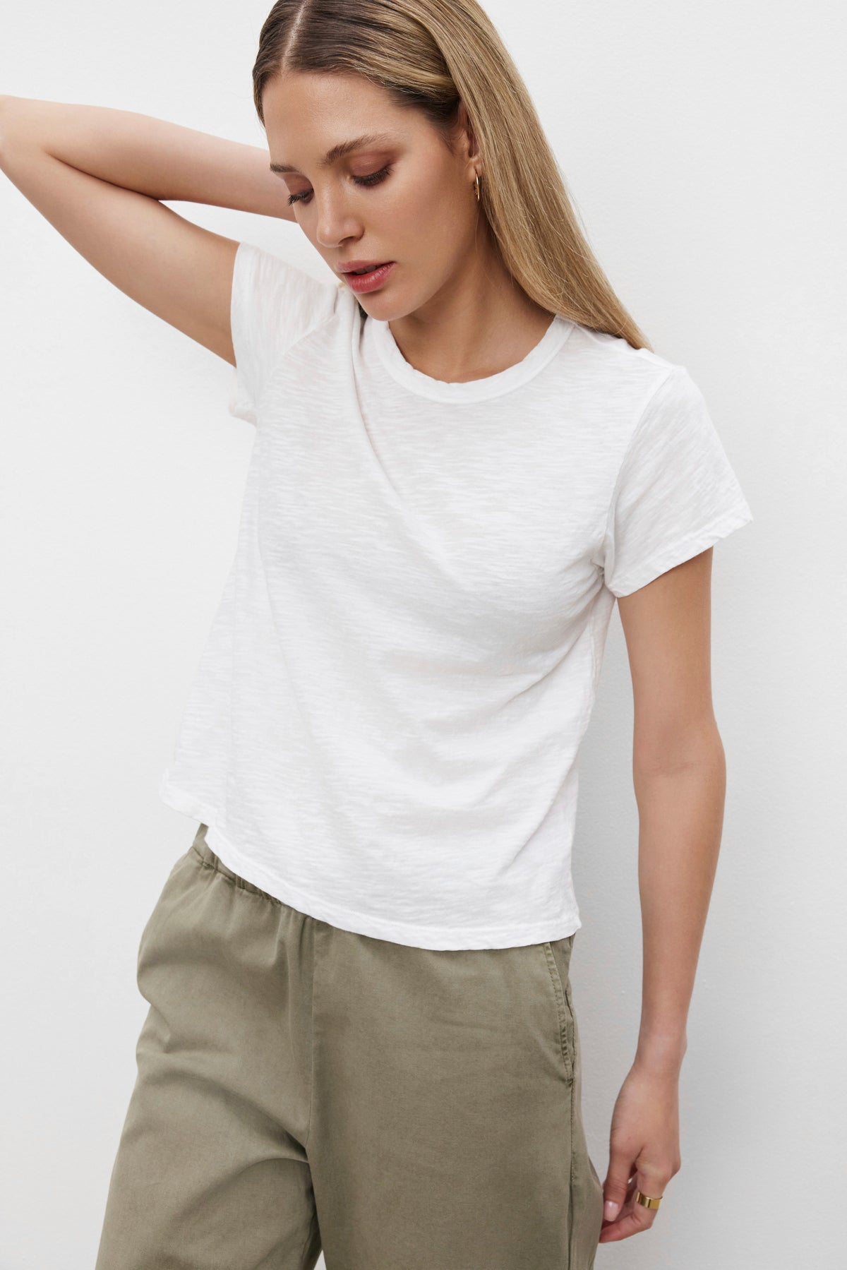   A person wearing a MARIE TEE from Velvet by Graham & Spencer and khaki pants stands with one arm behind their head against a plain background, perfect for a casual occasion. 