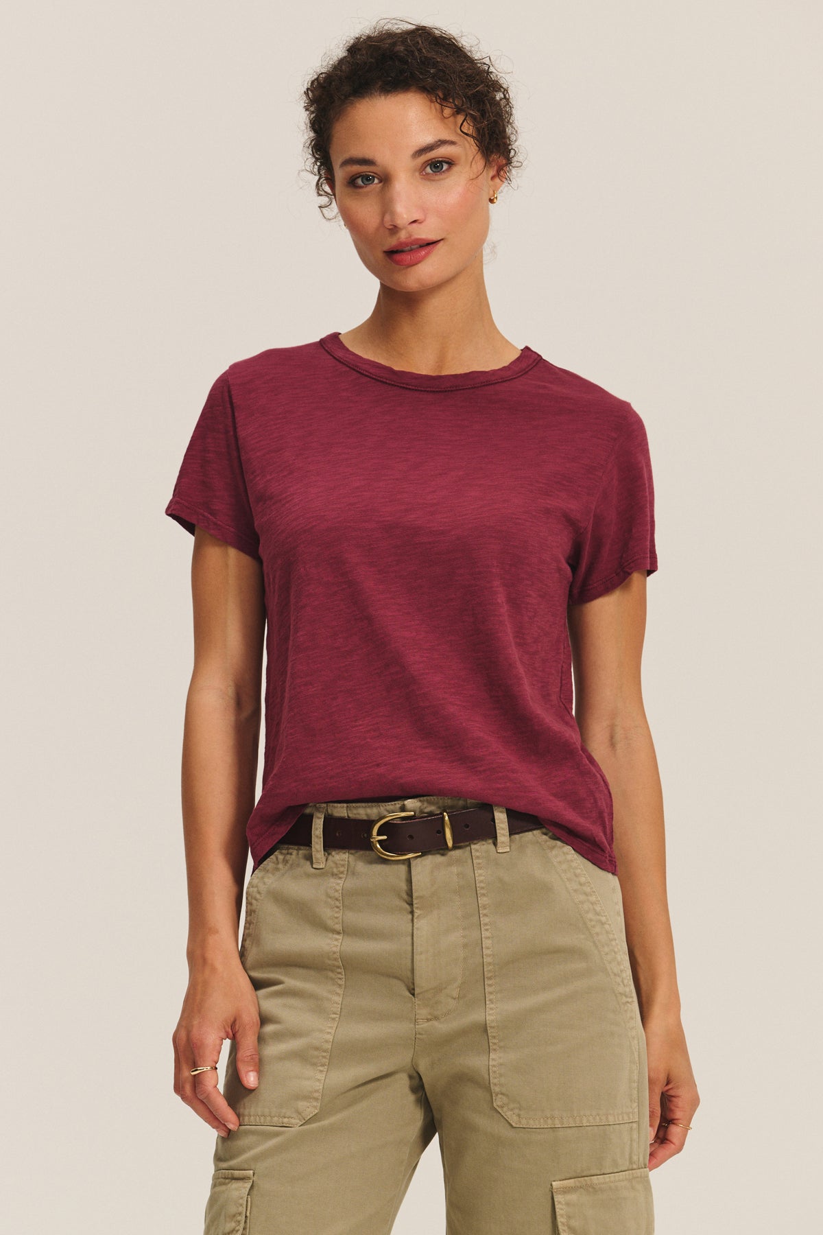   A person wears the Velvet by Graham & Spencer MARIKA TEE in maroon cotton slub with a relaxed boxy fit, tucked into high-waisted khaki cargo pants and a black belt, posed against a plain light background. 