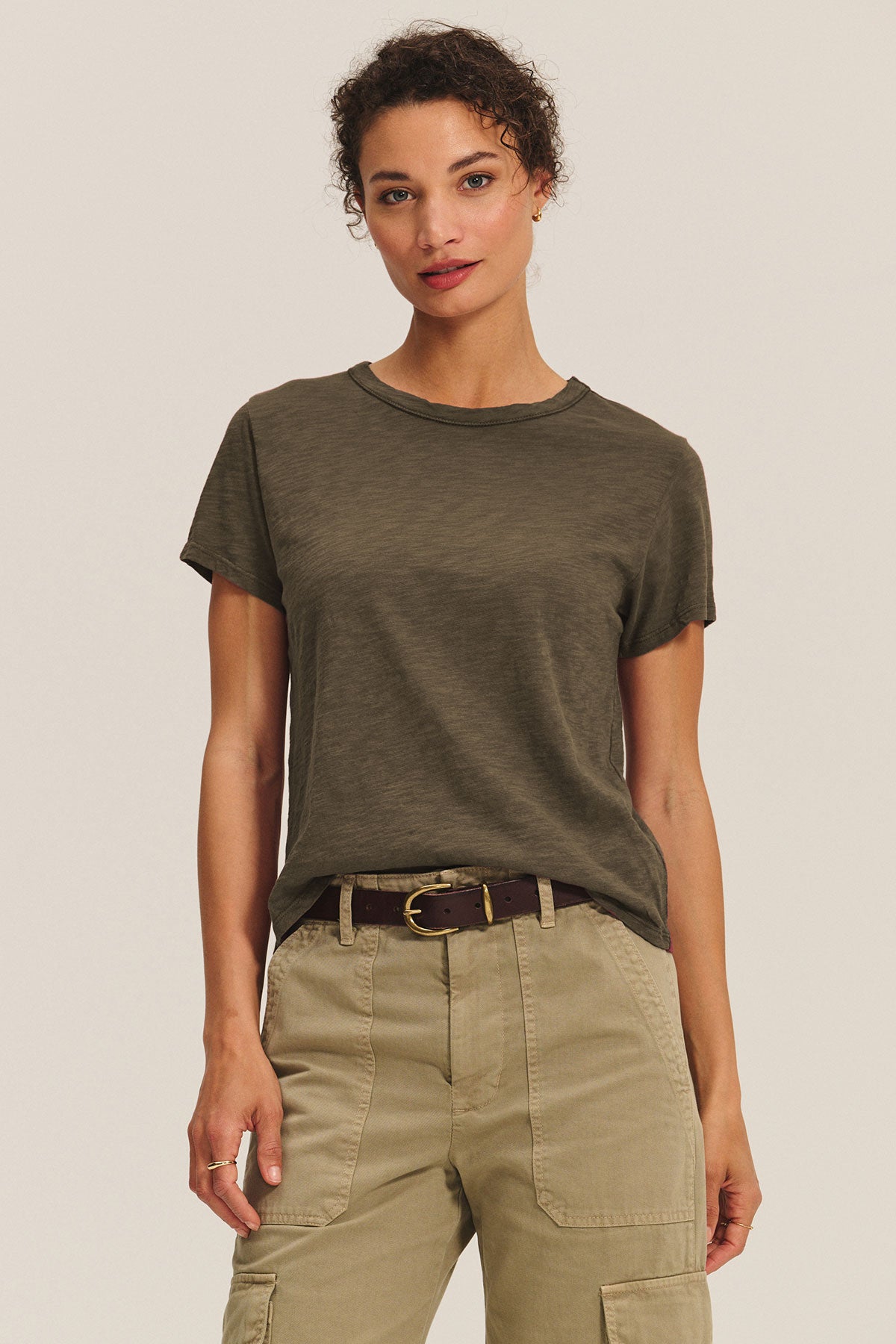 A person faces forward against a plain light background, wearing a boxy fit Velvet by Graham & Spencer MARIKA TEE in olive green cotton slub, tucked into belted khaki cargo pants.-40417104593089
