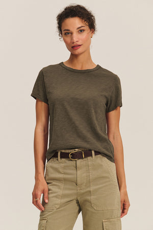 A person faces forward against a plain light background, wearing a boxy fit Velvet by Graham & Spencer MARIKA TEE in olive green cotton slub, tucked into belted khaki cargo pants.
