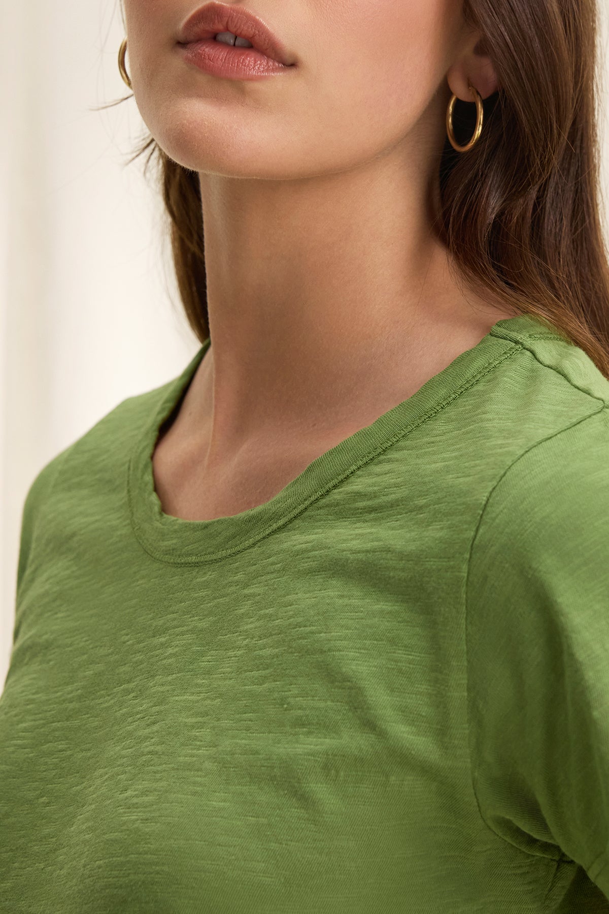   A person is shown from the shoulders up wearing a TILLY TEE by Velvet by Graham & Spencer paired with gold hoop earrings, embodying a classic California vibe. 