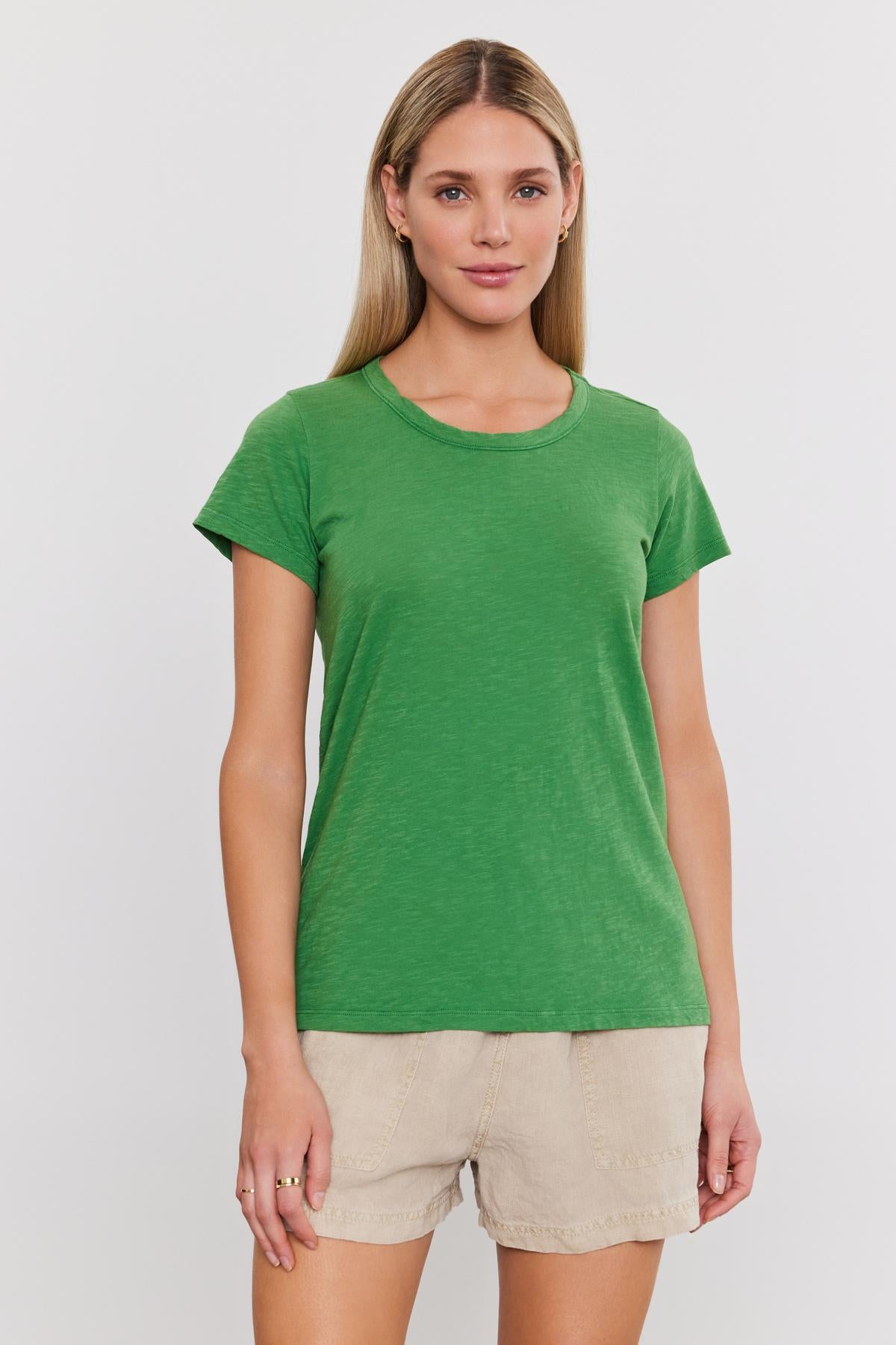   A woman stands facing forward wearing a green TILLY TEE by Velvet by Graham & Spencer and beige shorts against a plain white background. 