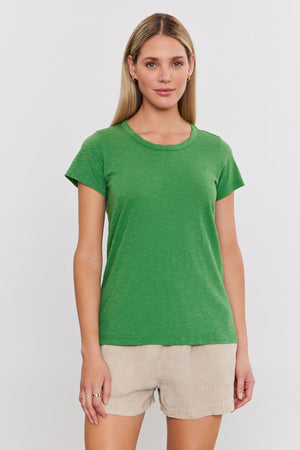 A woman stands facing forward wearing a green TILLY TEE by Velvet by Graham & Spencer and beige shorts against a plain white background.