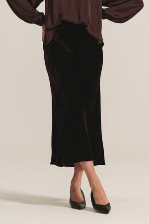 A person wears the FELICITY SKIRT by Velvet by Graham & Spencer, featuring silk velvet and an elastic waistband, paired with a loose long-sleeved blouse and black pointed-toe heels against a plain light background.