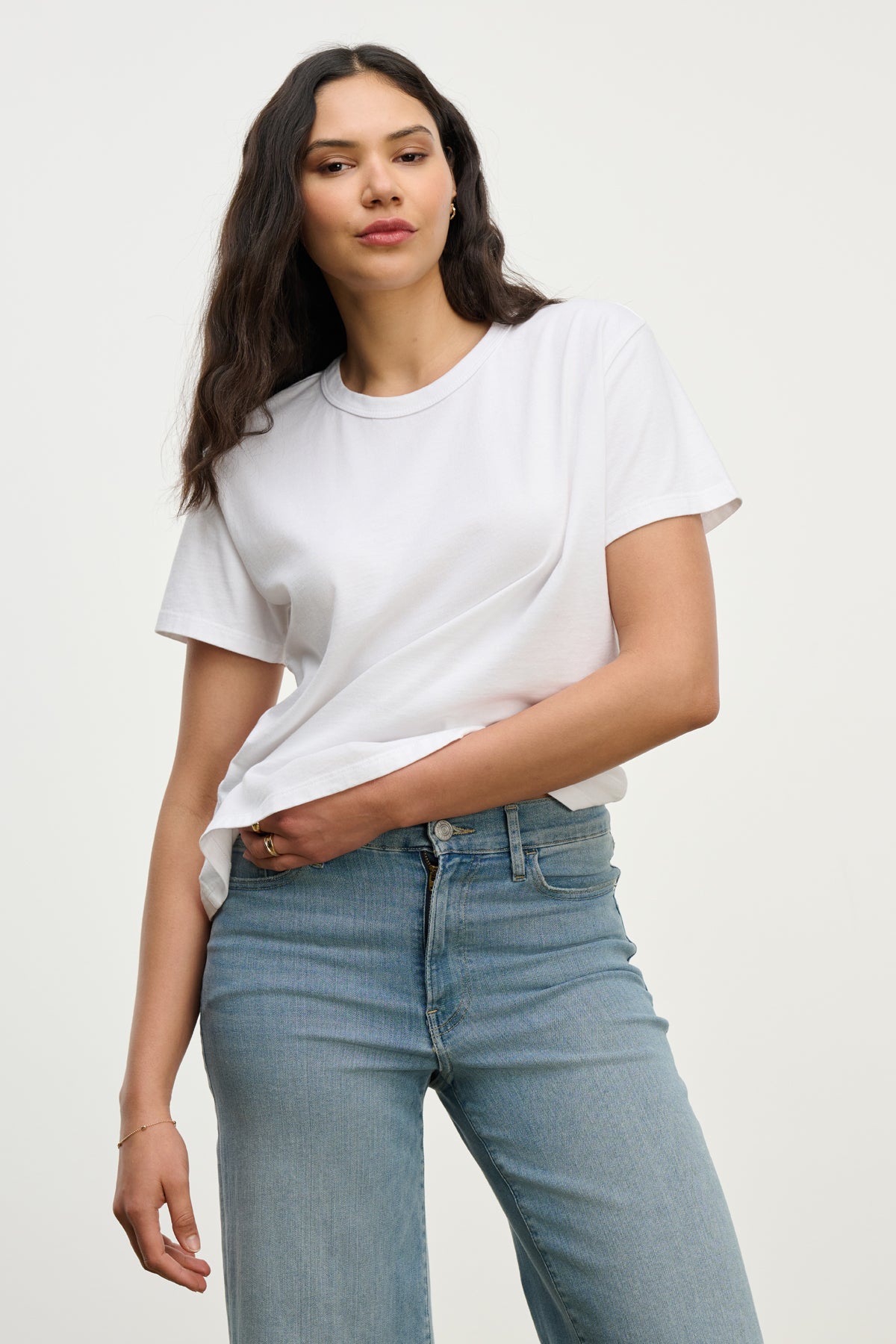 Someone wears the LEIGH TEE by Velvet by Graham & Spencer, a vintage-inspired cotton jersey top, paired with light blue jeans against a neutral background.-39725354025153