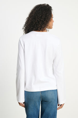 A person with curly hair wears the VEE TEE by Velvet by Graham & Spencer and blue jeans, standing with their back to the camera against a plain background.