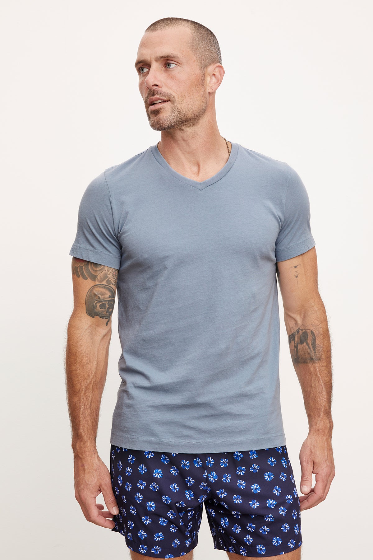   A man wearing a Velvet by Graham & Spencer MARSHALL V-NECK TEE and patterned shorts, standing against a white background with his arms at his sides. He has visible tattoos on both arms. 