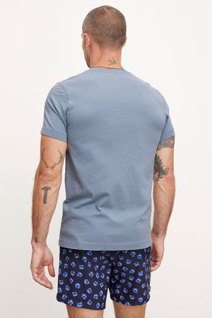 Rear view of a man wearing a gray Velvet by Graham & Spencer MARSHALL V-NECK TEE with patterned blue shorts, displaying visible tattoos on his arms and neck.